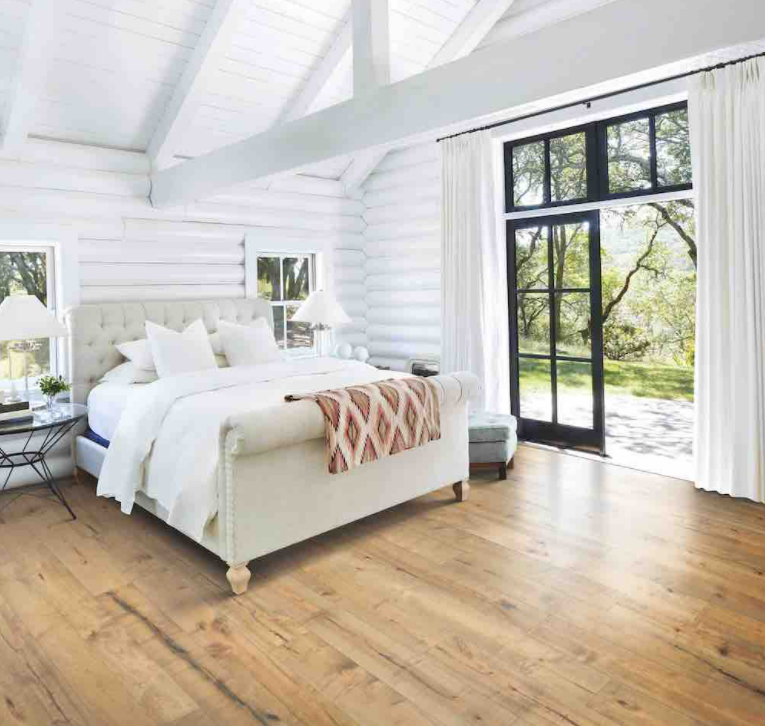 Karastan Hardwood flooring in rustic bedroom setting featuring white-painted brick walls, exposed wood beams, and open French doors